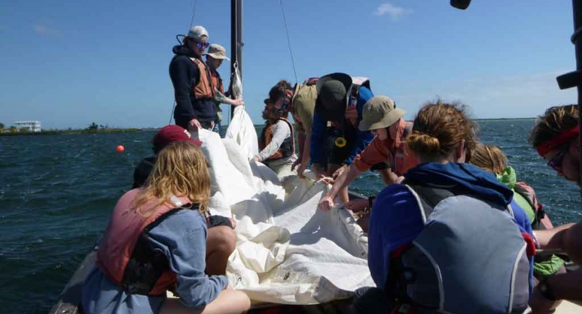 a group of people work on the fabric of a sail on a sailboat